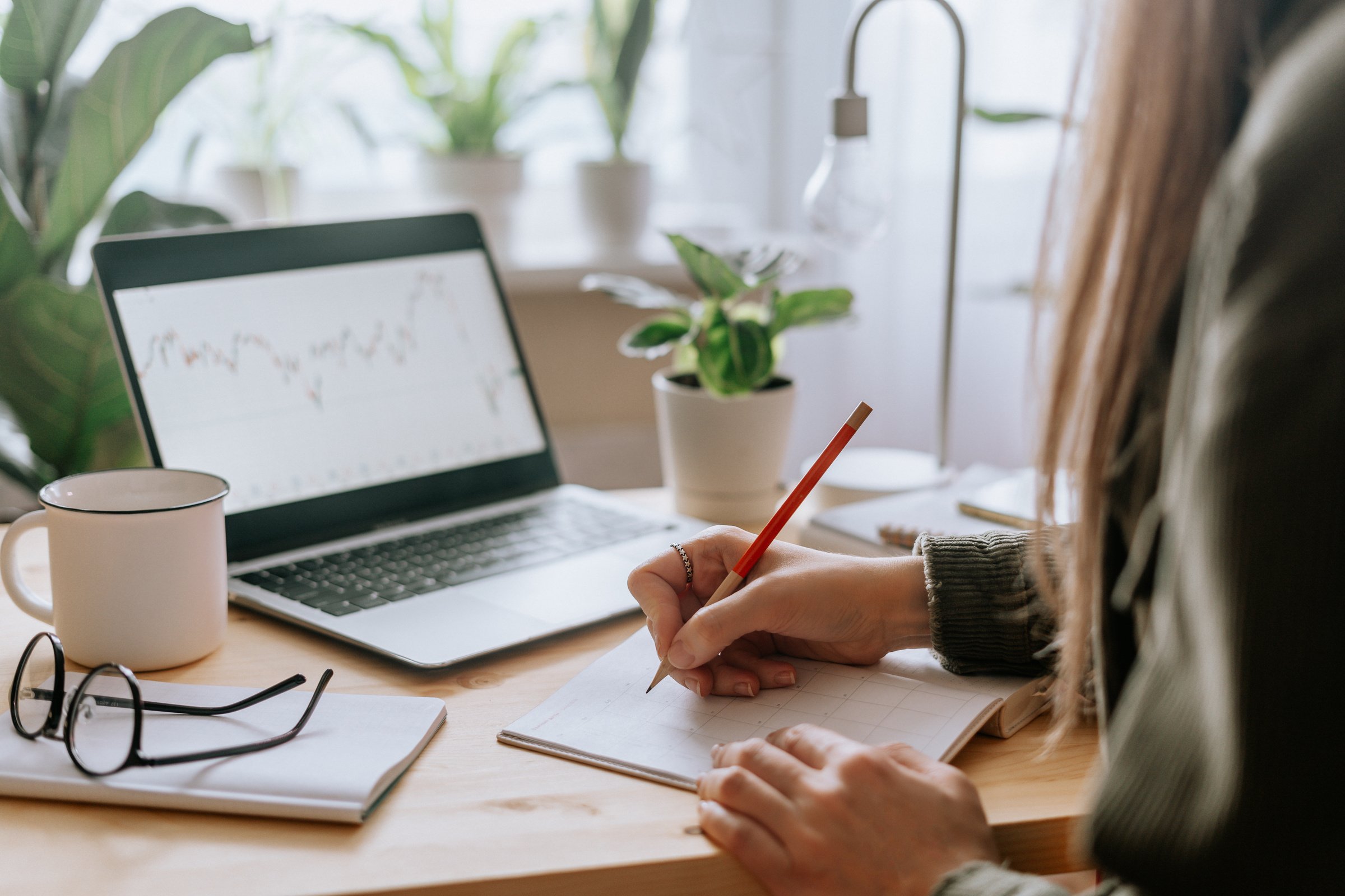 Woman writes in notebook with laptop